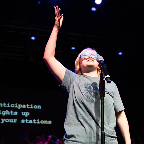 female participant reaches up with one hand while at a microphone
